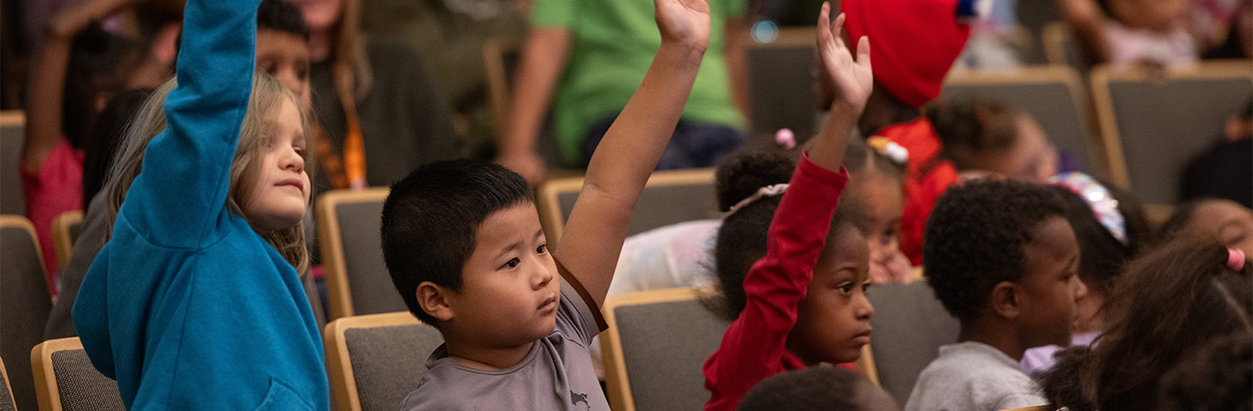 students raising their hands in the audience of an auditorium