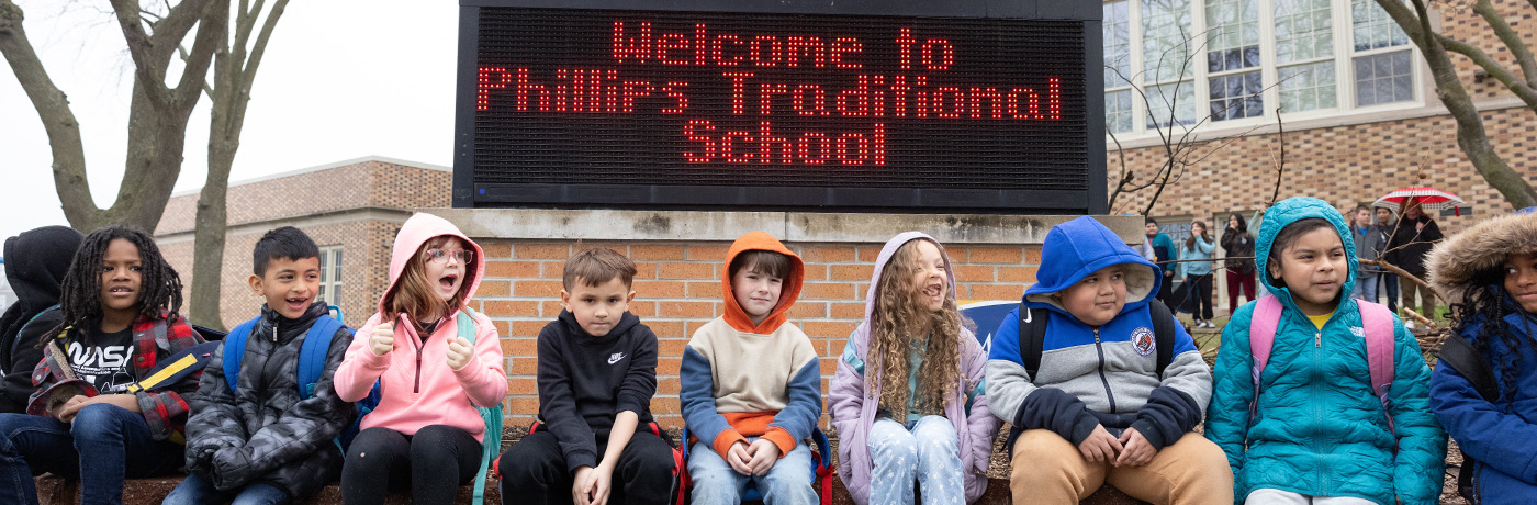 students sitting by schools sign